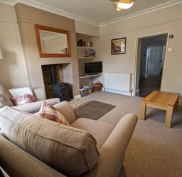 A living room with two sofas a wooden coffee table a wood stove and a television on shelves at The Cottage in Tetbury