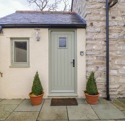 A small outdoor entrance with a green door and window flanked by two potted plants on a stone patio at Magnolia Barn in Mark