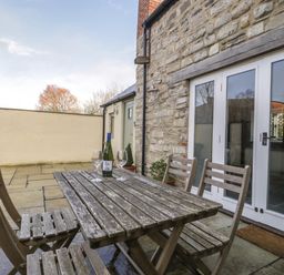 An outdoor patio with a wooden table and chairs next to a stone wall with glass doors at Magnolia Barn in Mark