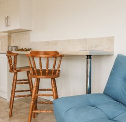 A kitchen area with wooden chairs and a blue sofa at The Stables in Crowcombe