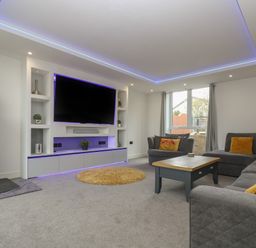 A living room with a large wall-mounted tv a fireplace and gray sofas at Valley View in Mullion