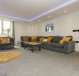 A living room with a large grey sofa yellow cushions coffee table and a round yellow rug at Valley View in Mullion