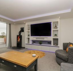 A living room with a wall-mounted TV a stove and a wooden coffee table at Valley View in Mullion