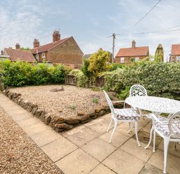 A garden patio with a white outdoor table and chairs next to a gravel area with plants at Tawny Cottage in Heacham