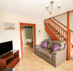 A living room with a sofa under stairs and television on a stand at Tawny Cottage in Heacham