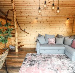 A living room with a grey sectional sofa with cushions wooden walls and a dining table with chairs at Offas Dyke Escape in St Asaph