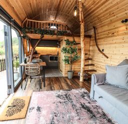 An interior wooden cabin with a kitchen area loft dining table chairs sofa and staircase at Offas Dyke Escape in St Asaph