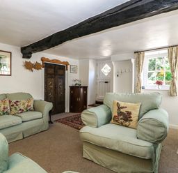 A living room with two armchairs and a sofa with decorative cushions a window with curtains and a door with hooks and a small cabinet at Small Piece in Porlock