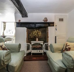 A living room with two cushioned armchairs facing a small electric stove under a black wooden mantel at Small Piece in Porlock