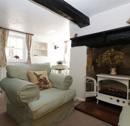 A living room with green armchairs a fireplace and windows with floral curtains at Small Piece in Porlock