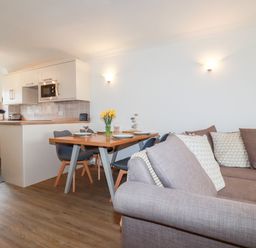 An open plan living space with a kitchen area a dining table with chairs and a sofa at 7 Europa Court in Mawgan Porth