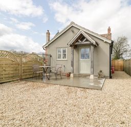 A small house with a gravel yard a patio with table and chairs and wooden fences at The Coal House at Mendip View in Wedmore