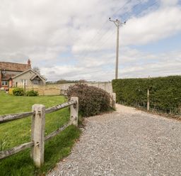 A gravel pathway next to a wooden fence and hedge with a brick house and garden in the background at The Coal House at Mendip View in Wedmore