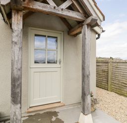 An exterior wooden door with glass panels under a wooden porch with a gravel path and wooden fence at The Coal House at Mendip View Wedmore