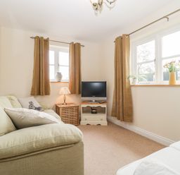 A small living room with a beige sofa cushions a lamp television and multiple windows with brown curtains at The Coal House at Mendip View in Wedmore