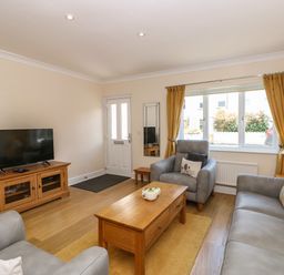 A living room with a television on a wooden stand a coffee table two armchairs a sofa and a window with yellow curtains at Inglewood in Keswick