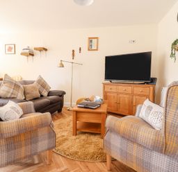 A living room with a TV on a wooden cabinet two armchairs and a sofa at Varley Villa in Newtown