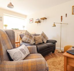 A living room with a plaid armchair a black leather sofa cushions a standing lamp and wooden shelves on the wall at Varley Villa in Newtown