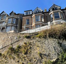 A row of houses on top of a stone retaining wall with railings and dry vegetation at Albany in Looe