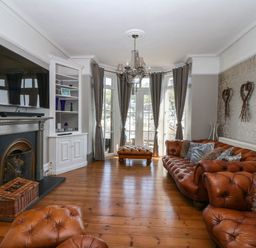 A living room with leather sofas a fireplace and large windows with curtains at Albany in Looe