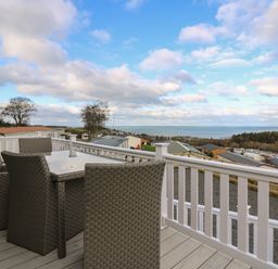 An outdoor deck with a table and four chairs overlooking houses trees and the sea at McAuliffe Lodge in Borth