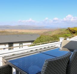 An outdoor terrace with a glass table and woven chairs overlooking a scenic landscape at McAuliffe Lodge in Borth