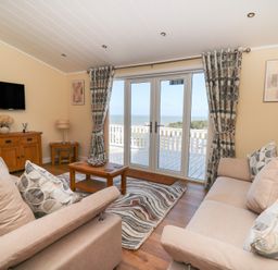 A living room with two sofas a coffee table and TV facing balcony doors with sea view at McAuliffe Lodge in Borth
