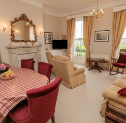 A living room with red chairs around a table and beige sofas by windows at Sandsend Sunset View in Whitby