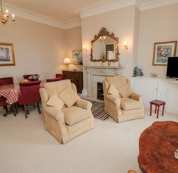 A living room with two beige armchairs a wooden coffee table a dining table with red chairs and a television at Sandsend Sunset View in Whitby
