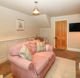 A sitting room with a pink sofa cushions a dining table wooden door and a wall-mounted television at Chapel Cottage in Corbridge