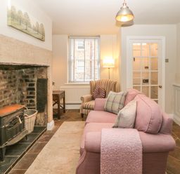 A living room with a fireplace a pink sofa and a striped armchair at Chapel Cottage in Corbridge