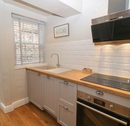 A kitchen with a wooden countertop sink electric stove oven and a window with blinds at Chapel Cottage in Corbridge