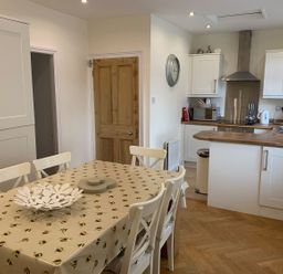 A kitchen with white cabinets a wooden countertop a dining table with chairs and a bee patterned tablecloth at A Stone's Throw in Alnmouth