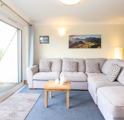 A living room with a gray sectional sofa and wooden coffee table next to sliding glass doors at Pavey Ark in Ambleside