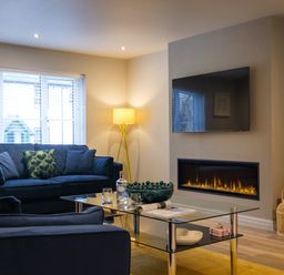 A living room with blue sofas a glass coffee table a corner floor lamp a wall-mounted television and a modern fireplace at The Neon Rose in Bowness-On-Windermere