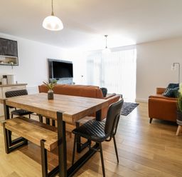An open plan living room and kitchen with wooden dining table and bench two leather sofas and a wall mounted TV at 2 Pensyflog Barns Porthmadog