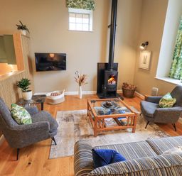 A living room with two armchairs a wood stove and a coffee table at Old Howgate Barn Outgate near Hawkshead