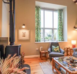 A living room with a wood stove sofa armchair coffee table and window with green curtains at Old Howgate Barn Outgate near Hawkshead