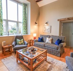 A living room with a striped sofa, armchairs, wooden coffee table, patterned curtains, and wall art at Old Howgate Barn Outgate near Hawkshead
