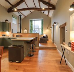 A kitchen and living area with wooden beams an island with stools and a window at Old Howgate Barn Outgate near Hawkshead