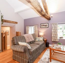 A sitting area with a striped sofa and wooden coffee table with plants and windows at Low Ashmead Cottage in Hawkshead