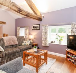 A living room with a striped sofa a wooden coffee table a television on a wooden stand and wooden ceiling beams at Low Ashmead Cottage in Hawkshead