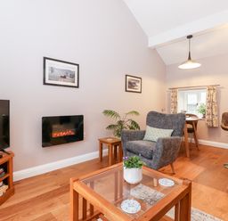A living room with a television a glass coffee table a gray armchair and a dining area at Low Ashmead Cottage in Hawkshead