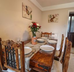A dining room with a wooden table set for four with plates glasses flowers and a bottle at Rayside in Ullswater