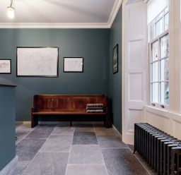 A hallway with a wooden bench stacked with blankets a radiator and three framed pictures on the wall at The Vicarage near Rosthwaite