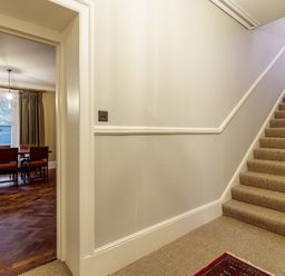 A staircase with carpet leading up and a dining room with a wooden table and chairs visible through a doorway at The Vicarage near Rosthwaite