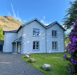 A white house with blue trim surrounded by grass and rocks with purple flowers on the side at The Vicarage near Rosthwaite