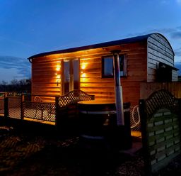 An exterior view of a wooden pod with lit lamps and a deck with lattice fencing at Stag Lodge Pod in Llanfair Caereinion