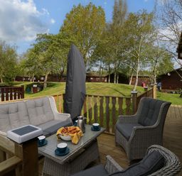 An outdoor wooden deck with rattan furniture including a table with croissants and coffee cups at Lakeland Dream at South Lakeland Leisure Lodge in Warton