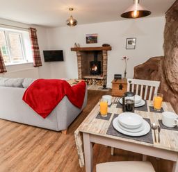 A living room with a dining table set with plates glasses and cutlery a grey sofa with a red throw a fireplace and a rock wall at The Old Mill Bake House in Goodrich